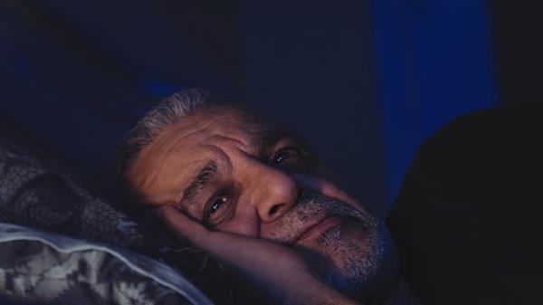 Elderly man can't sleep, lays awake in bed with eyes open, looking deep in thought